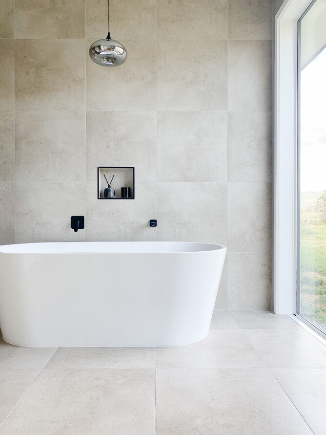 Freestanding bath beside full height picture window with overhanging pendant