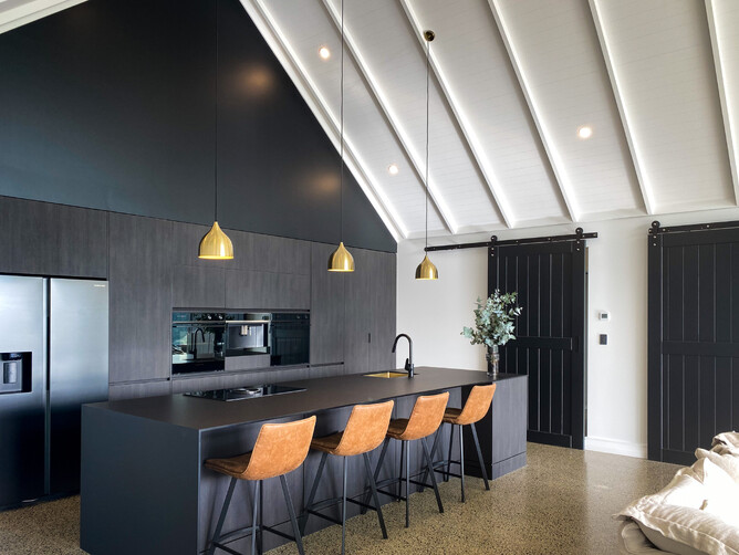 view of black kitchen and island from lounge area with rake ceiling