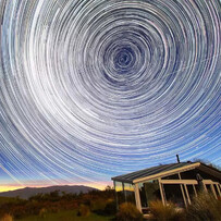 Star trails circling above a glass-roof cabin in the Mackenzie Region