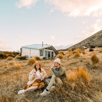 Guests relaxing outside a SkyScape cabin surrounded by tussock and hills