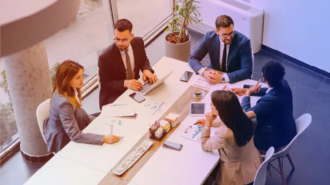 Photo of people in discussion around a meeting room table.
