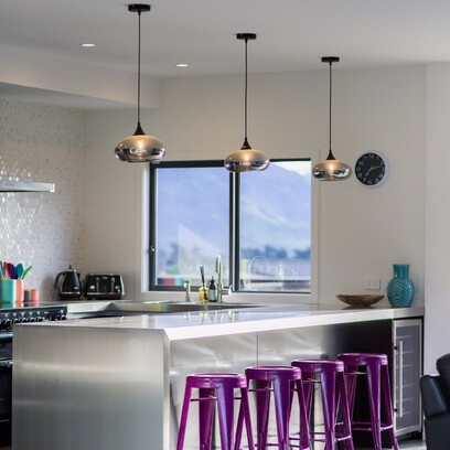 A light and bright kitchen with white bench tops, purple bar stools and feature pendant lights.