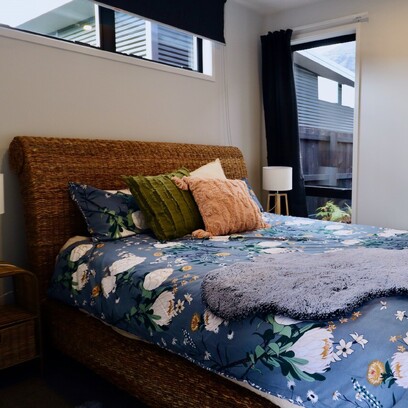 A cozy bedroom with a large bed, light walls, floral duvet and rattan headboard.