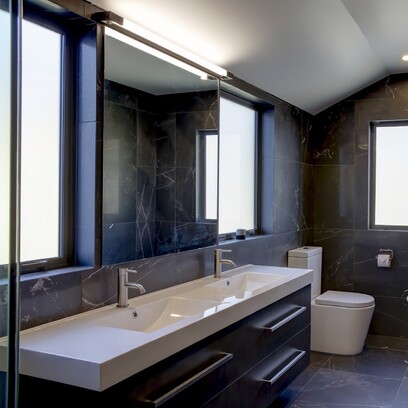 A dark grey tiled bathroom with large double vanity, mirror, and toilet.