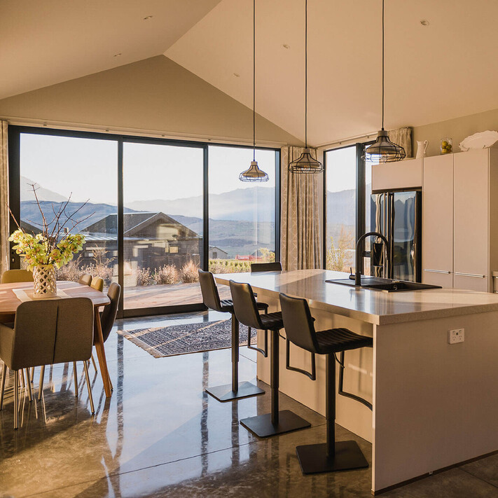 A stylish kitchen with polished concrete floor, pendant lighting, feature kitchen island and views from the large sliders at the front.