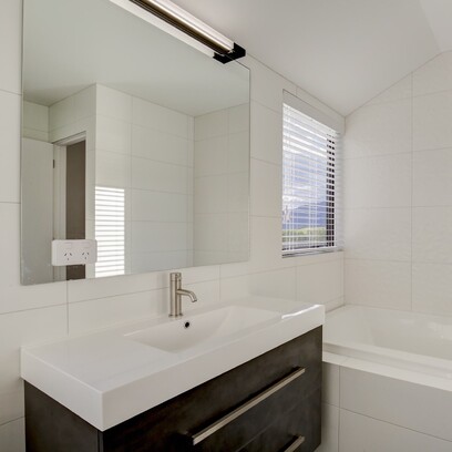 A fresh and modern bathroom with white tiled walls, dark vanity with light basin, large mirror and bath.