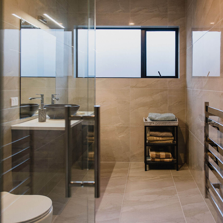 A luxurious tiled bathroom with glass shower, and lots of natural light.