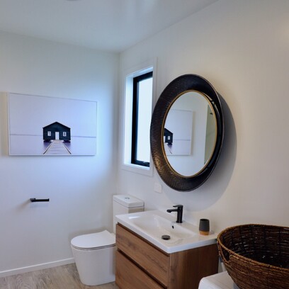 A compact yet clever bathroom with light walls, wood vanity with white top, and timber floors.
