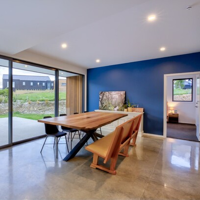 Dining area with s polished concrete floor, wood dining table and blue feature wall.