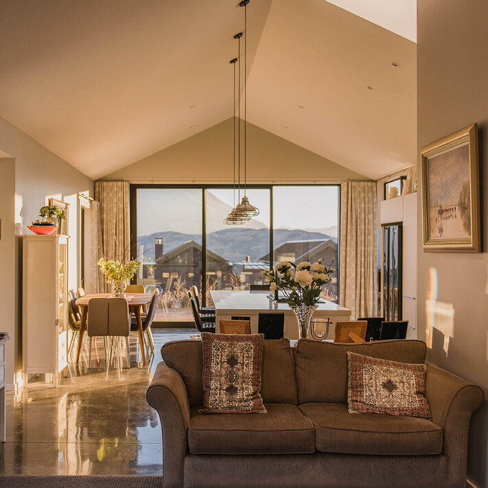 Looking out along the living and dining area of the home. Polished concrete floors, warm light and styled furniture.