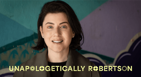 A portrait photo of Nicole Robertson, founder of Unapologetically Robertson, standing in front of a colourful wall.