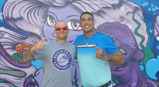 Sam Troth standing with a community leader in front of a mural, representing colour, creativity, and connection.