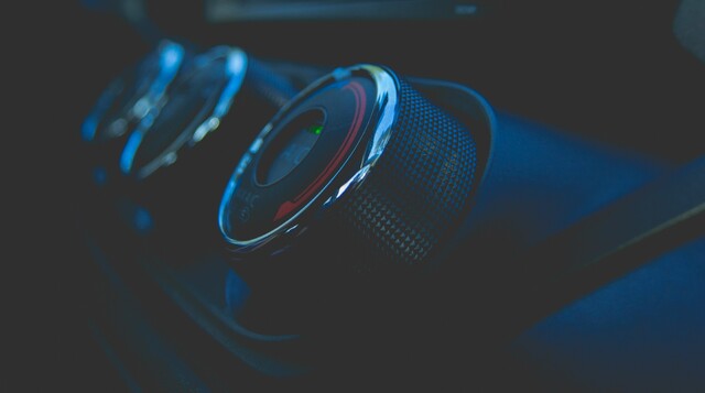 Close-up of a car’s air-conditioning and temperature control knobs with metallic texture, illuminated by soft blue lighting.