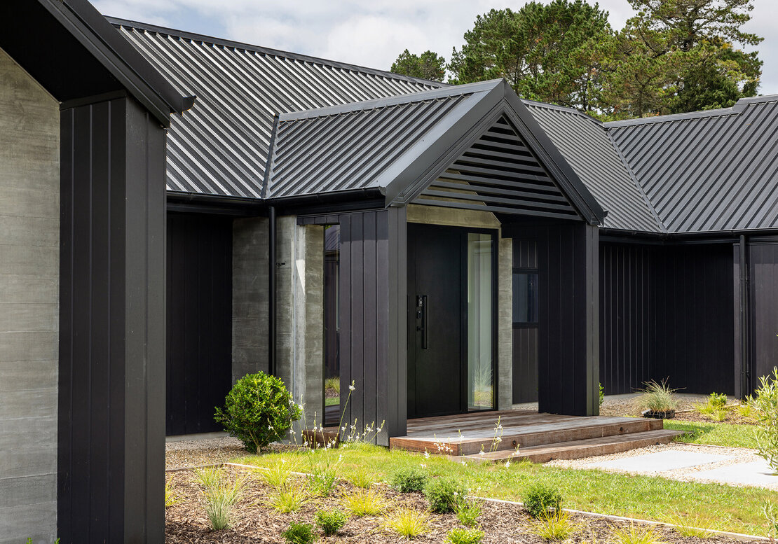 The image shows a new build completed by Straight Up Builders Tauranga, built in rural Katikati. The image shows a mid-shot of the exterior entry, cladding, and roof.
