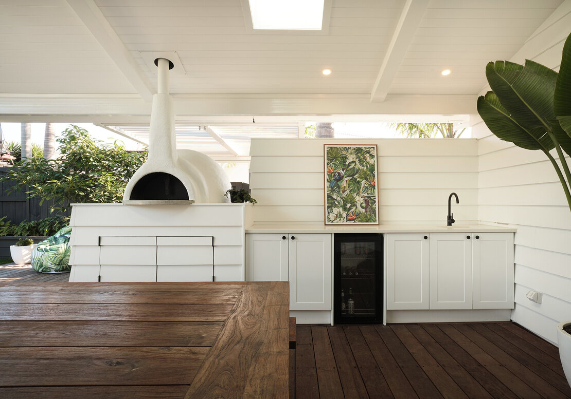 An enclosed outdoor kitchen area with pizza oven, kitchen bench with bar fridge.