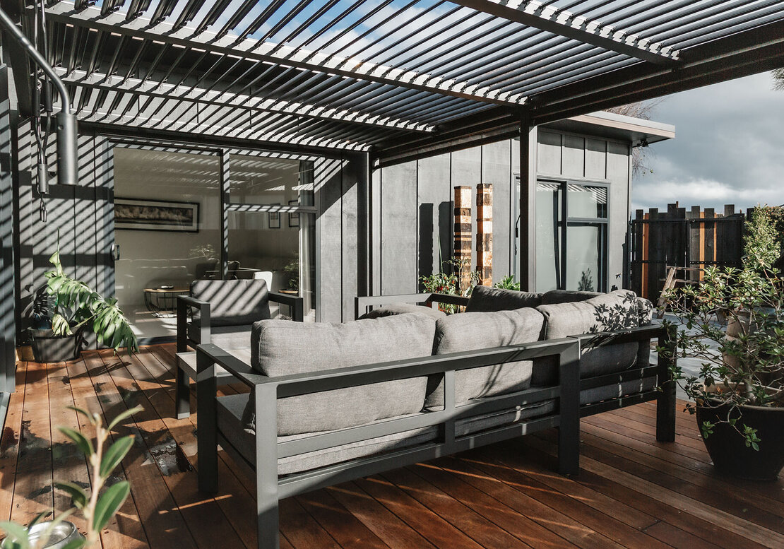 New deck, home, and pergola in black. Outdoor furniture has been placed on the new deck. The pergola louvres are open to let sunlight in.