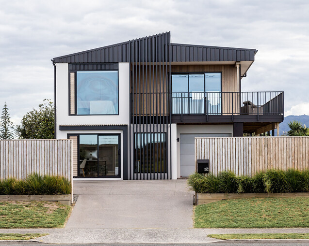 The image shows a full home renovation in Papamoa that was completed by local Papamoa Builders. The image shows the newly completed renovation, a modern home with large windows, new joinery, a deck, and cladding. This image shows the best builder's workmanship.