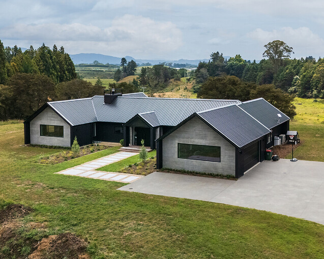 A new home built by builders in Tauranga. Situated on rural land with trees and hills in the distance. The home is grey and black, with a large driveway. The new home is a modern style featuring the best builder's workmanship.
