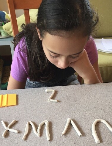 Young girl sitting at table with clay alphabet