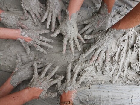 children's hands covered  in a clay, smearing clay on a surface
