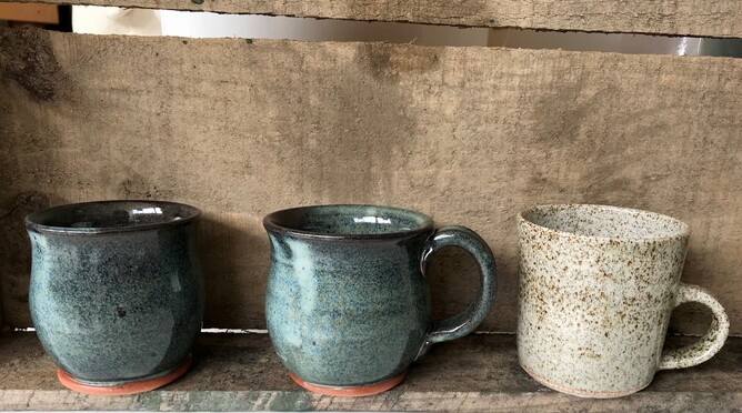 three small cups sit on a bare wood shelf. Two are blue ad one a speckled off white.