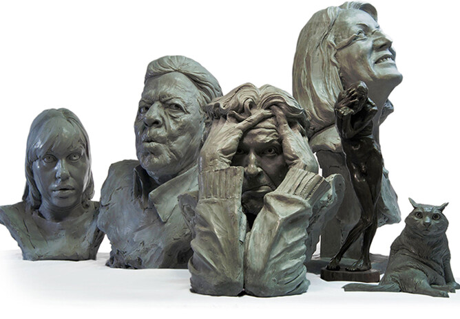 A selection of grey head sculptures against a white background. To the right of the heads there is a sculpture of a cat
