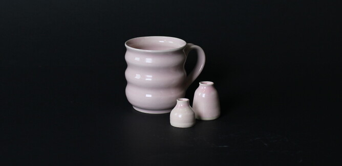 Image on black background of a pale pink mug with wavy waive-like edges and two tiny vases