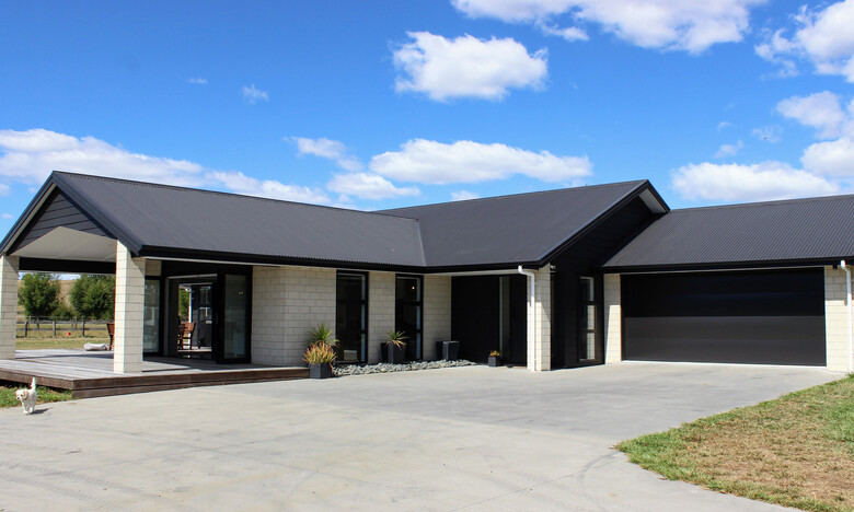 Image of large stone coloured brick home with dark roofing, doors and joinery. New home by Coull Builders, Otorohanga.