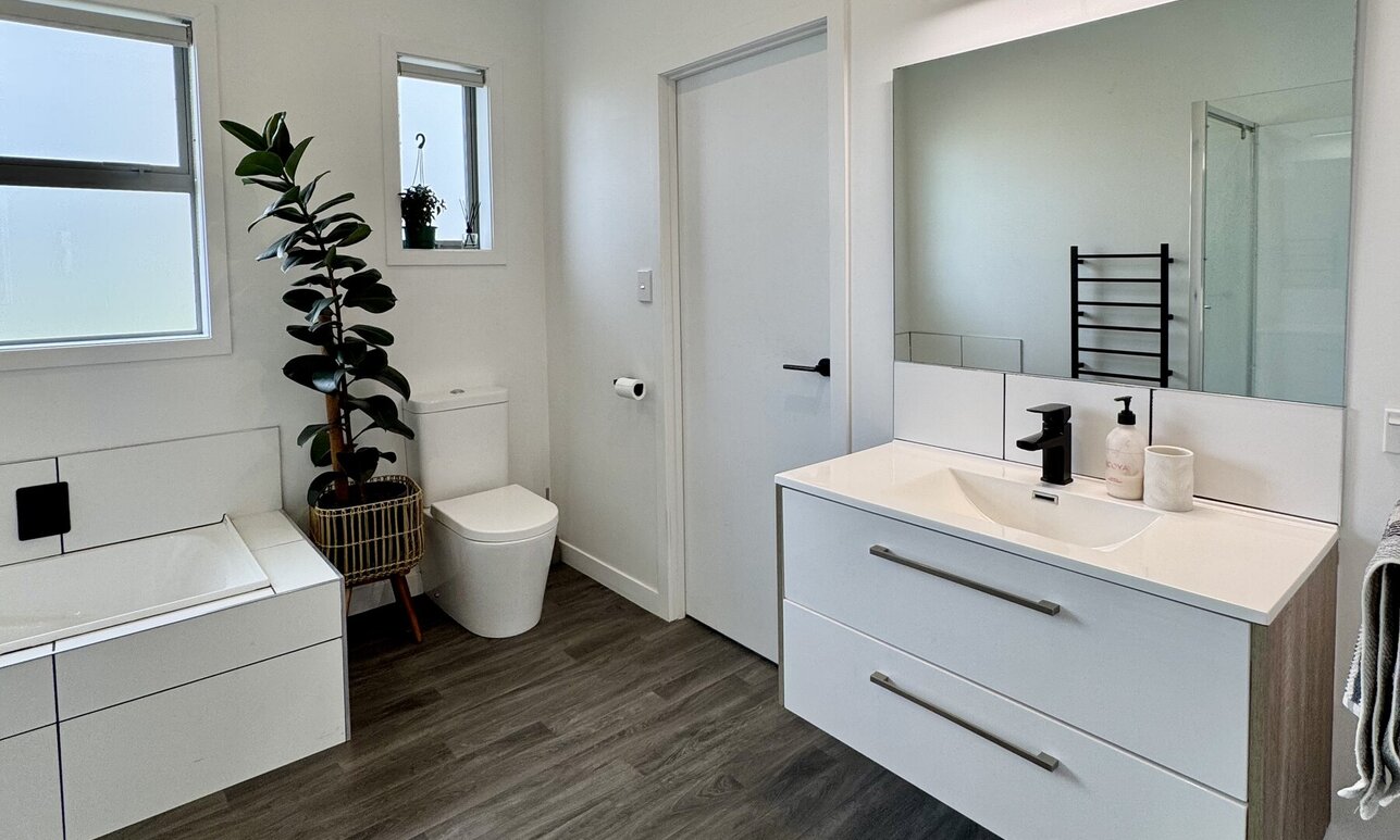 Fresh new white tiled bath, toiler and black tiled bathroom by Coull Builders, Otorohanga.