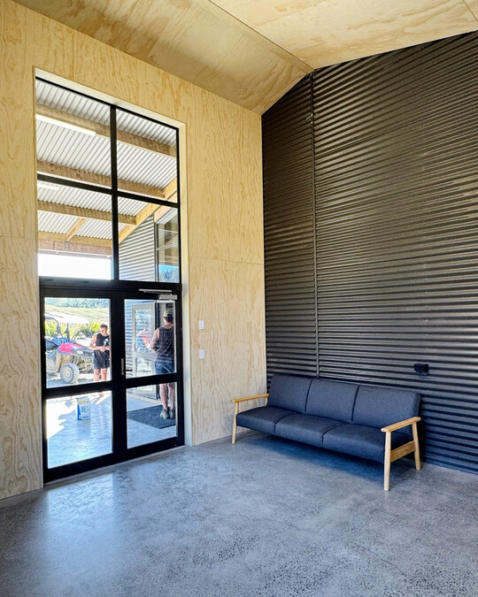 Office space interior lined with plywood, paired with large expansive windows with dark joinery. Coull Builders, Otorohanga.