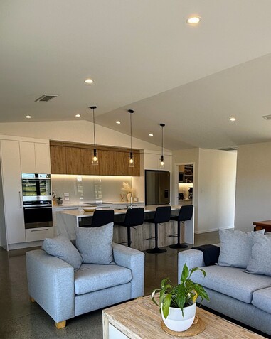 Image of newImage of light modern kitchen with timber accents, and peak of grey lounge suite. Building by Otorohanga builders, Coull Builders.