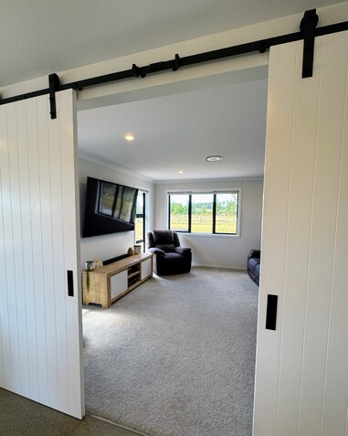 Image of large carpeted living space behind white slider doors. New home by Coull Builders, Otorohanga.