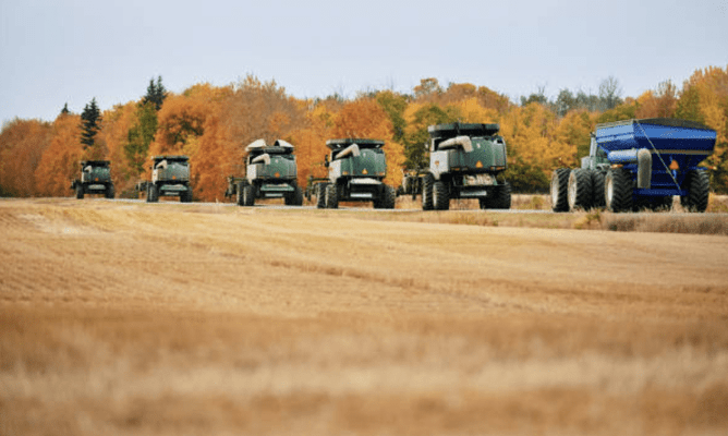 a line of agriculture vehicles on a road surrounded by dry fields