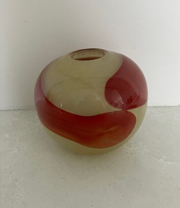 This is an early art glass vase by Ola H&ouml;glund and Marie Simberg-H&ouml;glund. It is a circular form in a creamy yellow base colour with a red swirl around the centre of the vase.