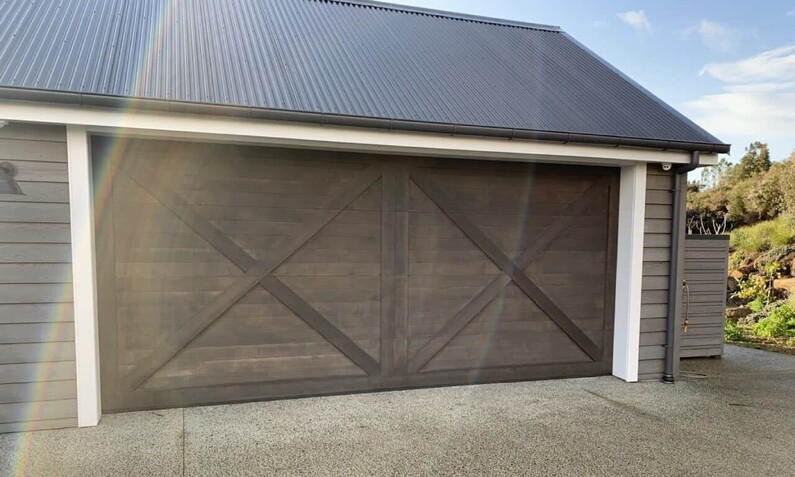 Photo of a timber garage door fitted to a home in Rodney, Auckland. Barn-style design.
