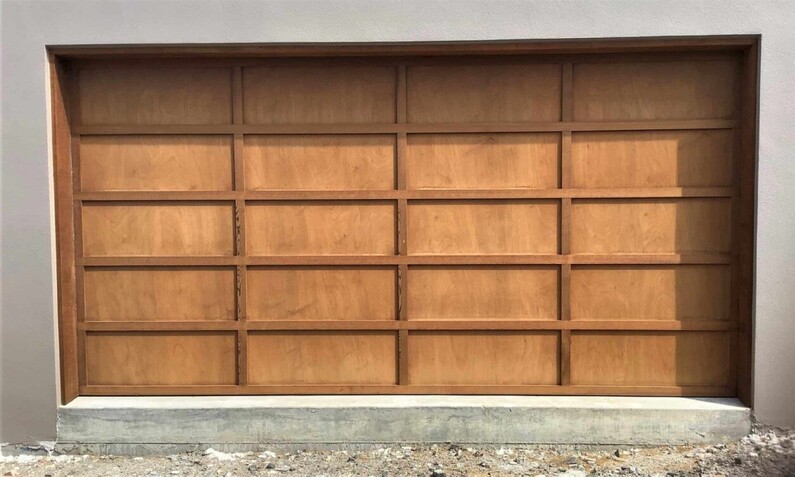 Photo of a Plywood and Batten (also known as board and batten) garage door fitted to a Rodney, Auckland home. Light brown finish. Panels arranged in a 4 x 5 pattern. Double garage door