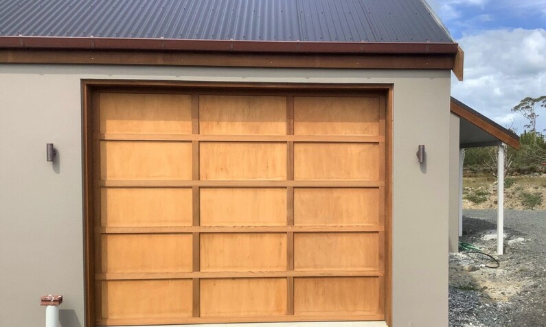 Photo of a light brown plywood/board panel garage door fitted to a Rodney, Auckland home. Boards are in a 3 x 5 pattern