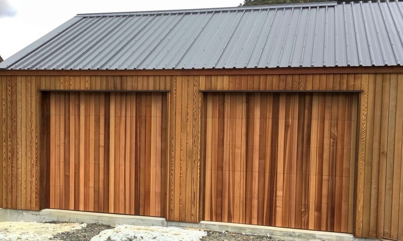 Photo of two timber garage doors fitted to a wooden house in Rodney, Auckland. Timber has a natural tone and is arranged vertically
