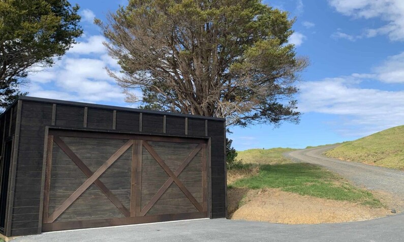 Photo of a timber garage door in the north Auckland countryside, dark stained wood, barn style doors with a criss-cross pattern