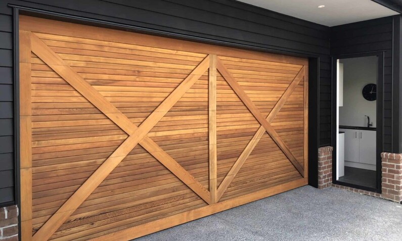 Photo of a timber garage door fitted to a home. Criss cross barn door pattern with light-brown coloured wood