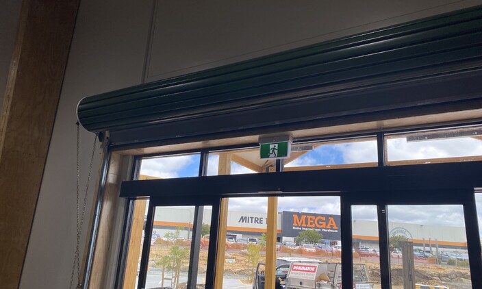 Photo of a roller door fitted to a storefront in Warkworth, Mitre 10 Mega in the distance.