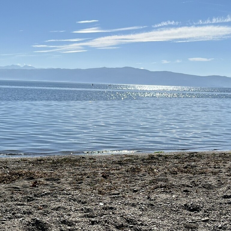 Lake Ohrid with the pebble beach in the foreground and mountains in the background.