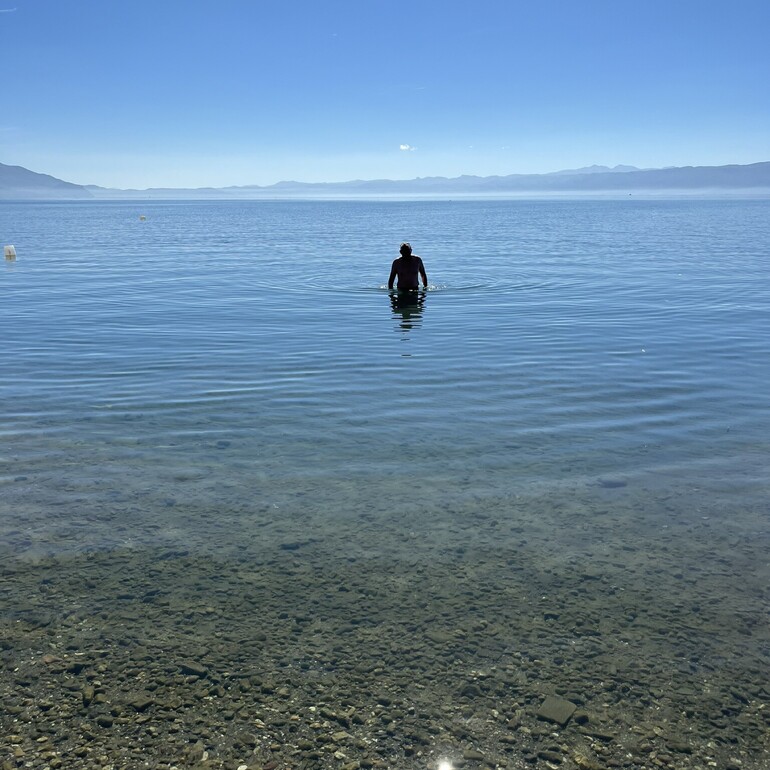 A man standing in the water of Lake Ohrid, walking towards the camera.