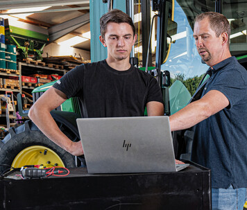 Technicians in a workshop reviewing Trimble precision guidance software on a laptop.