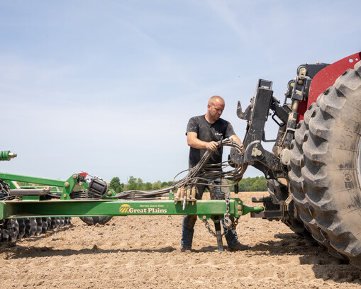 Farmer connecting an implement behind the tractor, hooking up cables