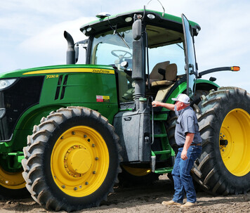 Farmer inside a John Deere tractor using Trimble auto-steering for hands-free operation.