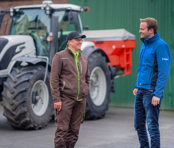 Trimble specialist consulting with a farmer beside a tractor, discussing GPS solutions.