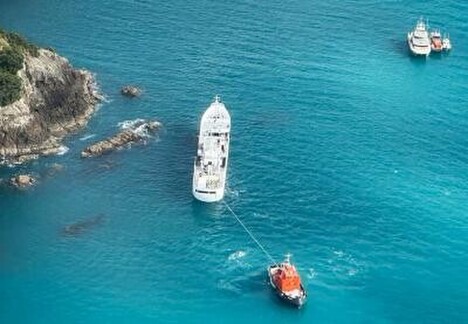 The Chokyo Maru aground on rocks at Motuhoropapa Island. An Auckland harbour tug is made fast to the vessel’s stern manoeuvring to refloat the grounded vessel.  Photo (c): NZ Herald | Michael Blampied
