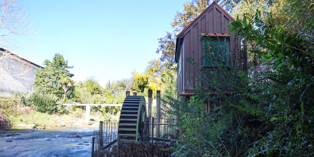 A flowing river with a water wheel next to it and a small wooden building on stilts