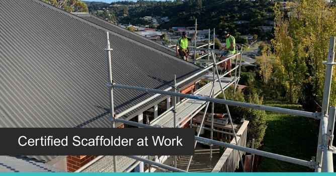 Two certified scaffolders working on rooftop scaffolding installation under clear skies.
